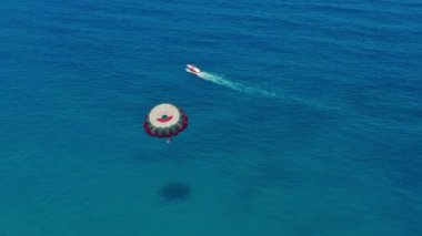 Havadan görünüm. Renkli bir paraşütle uçan insanlar motorlu bir tekne tarafından çekilsinler. Mavi gökyüzünde parasailing.