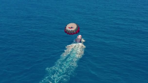 Aerial view. People flying on a colorful parachute towed by a motor boat. Parasailing in blue sky. — Stock Video