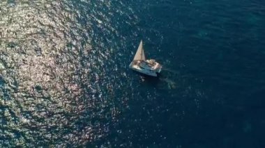 Hava görüntüsü. Katamaran denizden geçer, kamera yaklaşır ve geminin üzerinden uçar, günbatımında, güzel manzara.