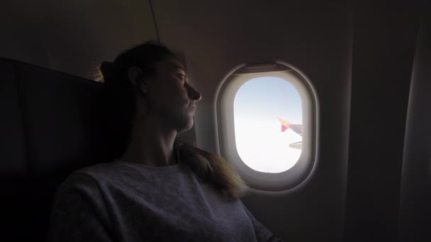 Dziewczyna w iluminator w płaszczyźnie. Młoda kobieta siedząca na siedzeniu pasażerskim i patrząc na okno na samolocie. — Wideo stockowe