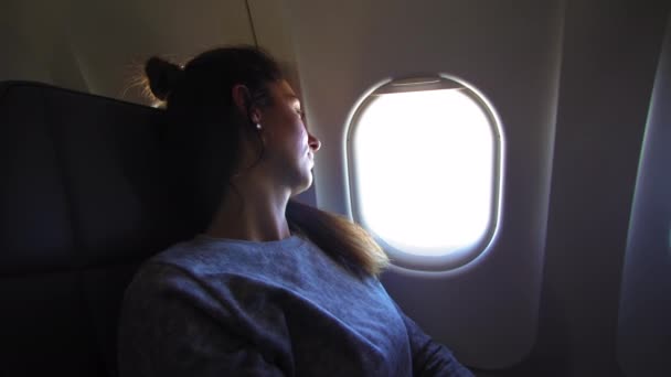 Το κορίτσι στην τρύπα στο αεροπλάνο. Νεαρή γυναίκα καθίσματα στο κάθισμα του συνοδηγού και κοιτάζοντας έξω παράθυρο στο αεροπλάνο. — Αρχείο Βίντεο