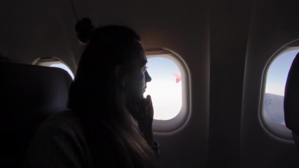 Девушка в иллюминаторе в самолете. Молодая женщина сидит на пассажирском сиденье и смотрит в окно самолета . — стоковое видео