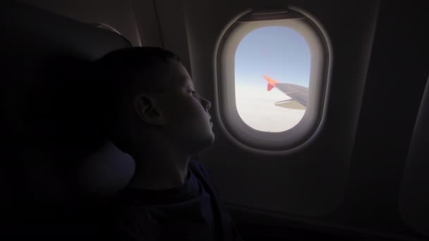 Der kleine Junge blickt zum Flugzeugfenster zum Flügelflugzeug. — Stockvideo