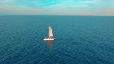 Hava görüntüsü. Katamaran denizden geçer, kamera yaklaşır ve geminin üzerinden uçar, günbatımında, güzel manzara