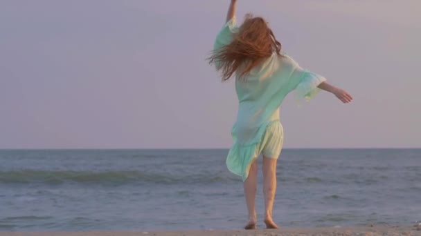 Zorgeloze vrouw dansen op de zonsondergang op het strand van de zee. Meisje spinnen. — Stockvideo