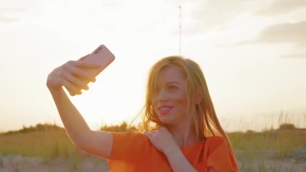 Lány lesz kész arra, hogy selfie a strandon naplemente, közelről. Rögzítő haj és korlátozás elintézés-ból fényképezőgép telefon fiatal asszony felkészül-hoz csinál mozi vagy video-ból maga-ra tenger háttér. lassított mozgás. — Stock videók