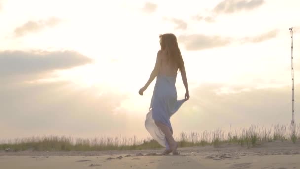 Unbekümmerte Frau, die am Sonnenuntergang am Strand tanzt. Mädchen beim Spinnen. Weiblichkeit bei Sonnenuntergang. Zeitlupe. — Stockvideo