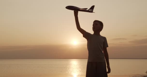 Niño feliz jugando con el avión de juguete contra el sol naranja verano. Mejor concepto de infancia . — Vídeo de stock