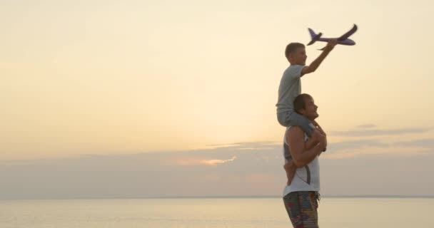 幸せな父と息子は、屋外を歩く夕日の幸せな家族で一緒に飛行機のおもちゃで遊ぶ. — ストック動画