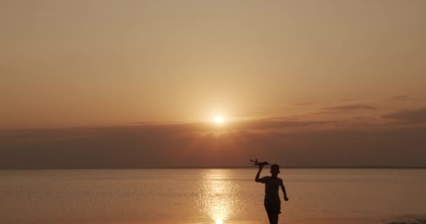 Criança feliz corre com um avião de brinquedo em um fundo de pôr do sol no mar . — Vídeo de Stock