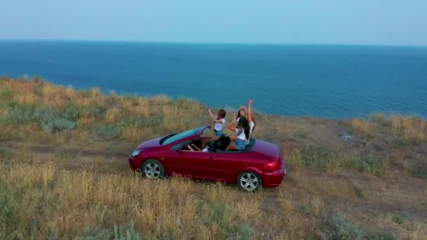 Αεροφωτογραφία. Νεαρά κορίτσια που οδηγούν κάμπριο αυτοκίνητο στο ηλιοβασίλεμα δίπλα στην παραλία μπροστά στη θάλασσα. Καλοκαιρινή περιπέτεια. — Αρχείο Βίντεο
