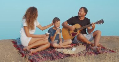 Aile akşam sahilde oturan ve gitar çalıyor.