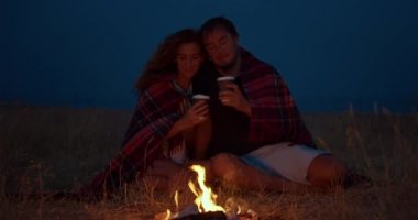Romantik çift geceleri bir kamp ateşi etrafında oturan.