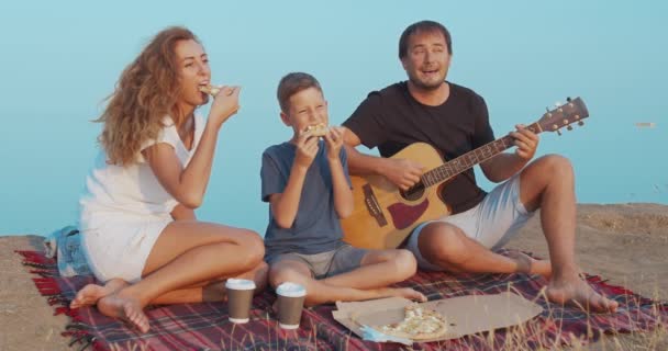 丘の上でピクニックをしながら、コーヒーやピザとスナックを食べながら、積極的にコミュニケーションをとる家族. — ストック動画