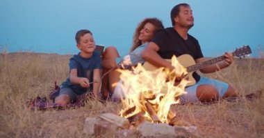 Baba gitar çalar , anne oğlu ile zevk ise şenlik ateşi yakınında aile pikniğinde dinlenirken. Close.