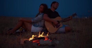 Şenlik ateşinin yanında oturan genç bir çift, gitar çalan adam. Romantik müzik ve mutlu çift ilişkileri. Gitar ile Romance çift.