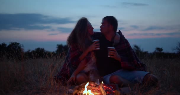 たき火の近くで一緒にデートする若い美しいカップル。ピクニックでボーイフレンドとガールフレンド。彼らはキスをし、抱きしめ、お互いに愛し合う。リレーションシップの概念. — ストック動画