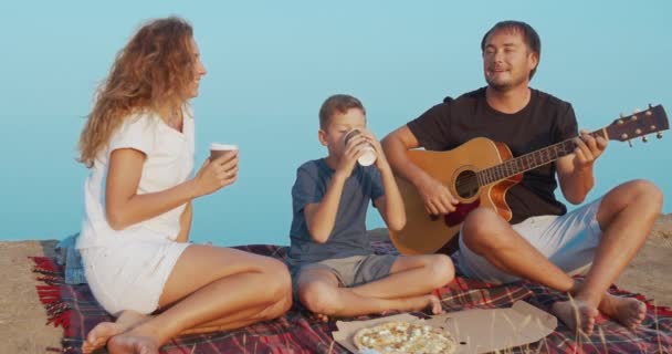 Familia comunicándose activamente y sosteniendo vasos con bebidas durante el picnic en una colina . — Vídeo de stock