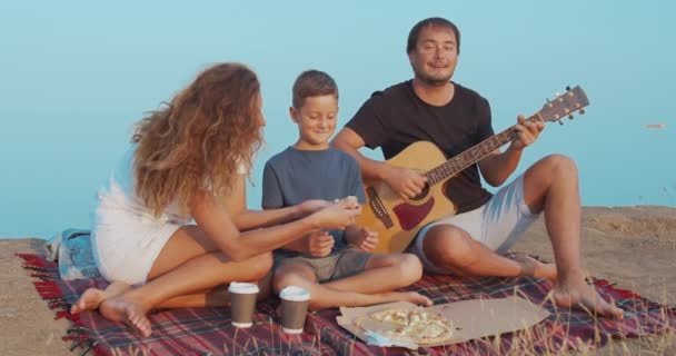 Familj kommunicerar aktivt medan picknick på en kulle och med mellanmål med kaffe och pizza. — Stockvideo