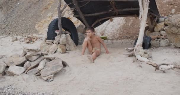 ケイブマン 男らしく男らしく屋外で面白い若い原始少年。進化生存の概念。岩場の集落に座って外の落ち着いた少年。先史時代の部族の男. — ストック動画