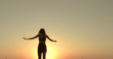 The girl jumps on trampoline in sunset sunlight on the beach.