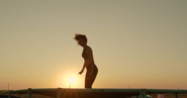 The girl jumps on trampoline in sunset sunlight on the beach.