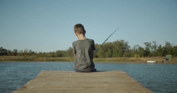 El chico está pescando en el viejo muelle del río. . — Vídeo de stock