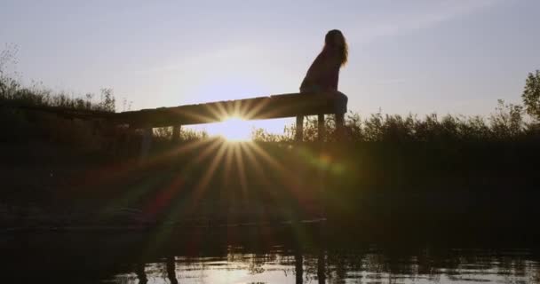 Menina bonita contempla o lago sentado no cais . — Vídeo de Stock