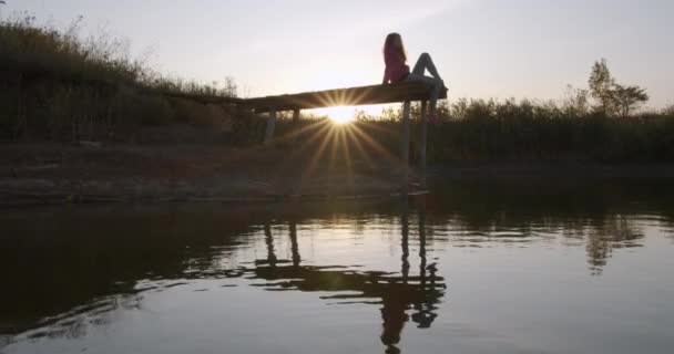 Menina bonita contempla o lago sentado no cais . — Vídeo de Stock