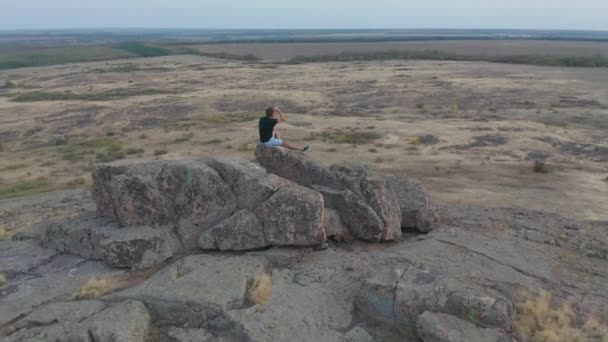 Вид з повітря. Літаючи навколо молодого чоловіка, що стоїть переможно на вершині гори на заході сонця . — стокове відео