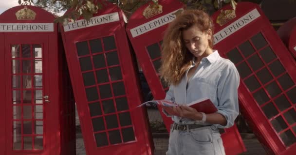 Attraktives Mädchen, das auf einem Hintergrund roter britischer Telefone läuft. Reisen, touristische Orte Konzept. — Stockvideo