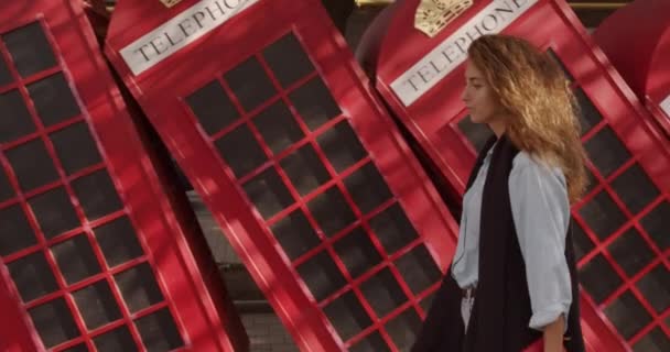 Attraktives Mädchen, das auf einem Hintergrund roter britischer Telefone läuft. Reisen, touristische Orte Konzept. — Stockvideo