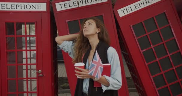 Muchacha atractiva caminando sobre un fondo de los teléfonos británicos rojos. Bebidas café y visitas turísticas . — Vídeo de stock