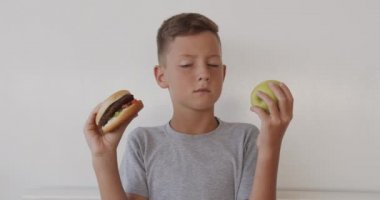 Boy choosing healthy or unhealthy food. Boy making a choice between apple and burger, healthy or fast, junk food, chose apple. Useful or harmful lifestyle.