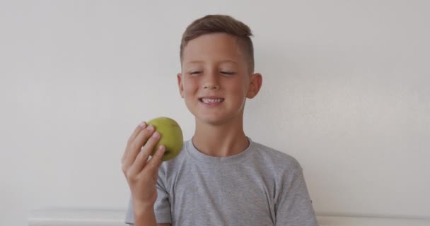 Крупним планом портрет хлопчика їсть смачне зелене яблуко і дивиться на камеру . — стокове відео