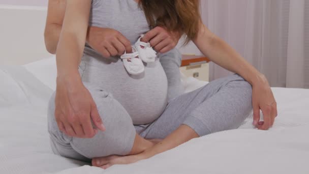 Schwangere tritt mit kleinen Babyschuhen auf ihren großen nackten Schwangerschaftsbauch. Die werdende Mutter spielt mit dem ungeborenen Kind. Pränatale Versorgung und Schwangerschaftskonzept für Frauen. — Stockvideo