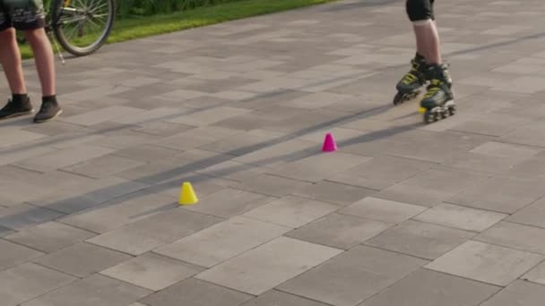 Le gambe ravvicinate di un giovane uomo pattinano professionalmente tra i coni in un bel tramonto serale in un parco cittadino . — Video Stock