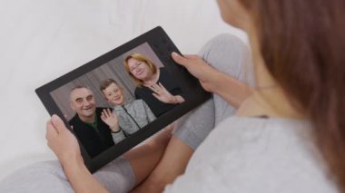 Evde dijital tablet kullanan genç bir kadının olgun anne babasıyla ve oğluyla konuşurken koltukta dinlenmesi. Mutlu aile.