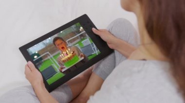 Küçük bir çocuğun doğum gününde pastaya mum üflediği videoyu izlediği akıllı telefon cihazını tutan genç kadının omzunun üstünden bakın. Yakın çekim..