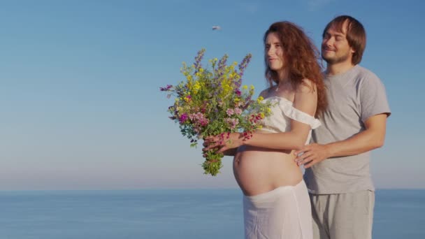 Junges schwangeres Paar umarmt und hält Bauch. Mama und Papa glücklich lächelnd friedlich, während kümmern Baby, Schwangerschaft in der Nähe des Meeres. — Stockvideo