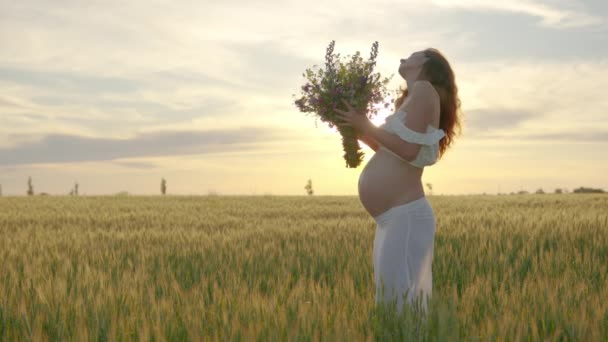 Zwanger meisje dansen in een veld met een boeket van bloemen. — Stockvideo