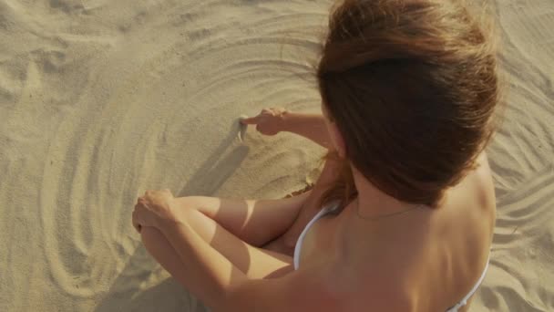 Вагітна дівчина сидить на пляжі в піску малює символ серця в піску . — стокове відео