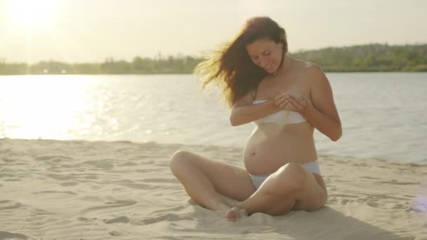 Una donna incinta sulla spiaggia. Versati della sabbia sullo stomaco. Pancia di donna incinta. Concetto di gravidanza. Primo piano di ragazza con la pancia nuda. Aspettativa del bambino . — Video Stock