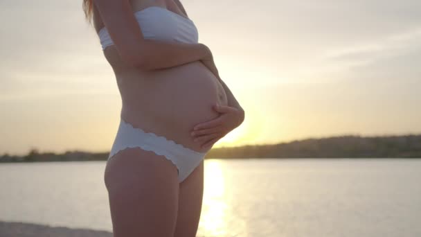 Hermosa mujer embarazada acariciando su vientre. Una mujer tocándose la barriga. Feliz madre embarazada en el mar. Primer plano. . — Vídeos de Stock