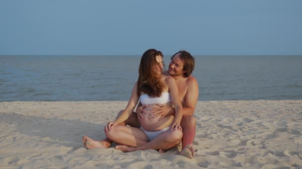 Беременная пара обнимается в море вместе. Счастливый муж с животом беременной жены в море. Муж мягко гладит беременную жену животик . — стоковое видео