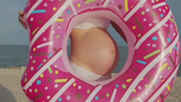 Bauch einer schwangeren Frau in einem rosa aufblasbaren Donut. Nahaufnahme. — Stockvideo