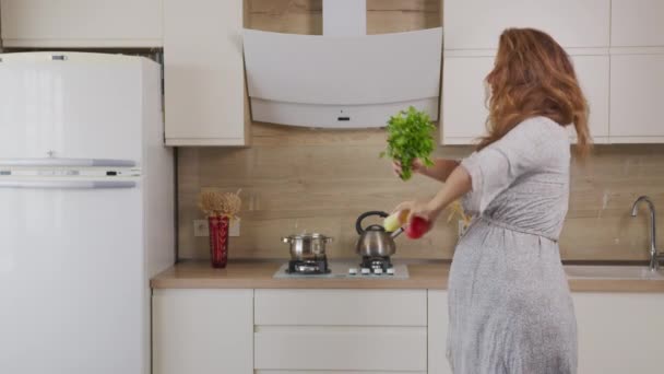 Tasasız, mutlu genç kadın ev hanımı modern mutfakta tek başına yemek pişiriyor, neşeli, aktif bir kız evde sağlıklı sebze salatası hazırlıyor müzik dinleyerek eğleniyor.. — Stok video