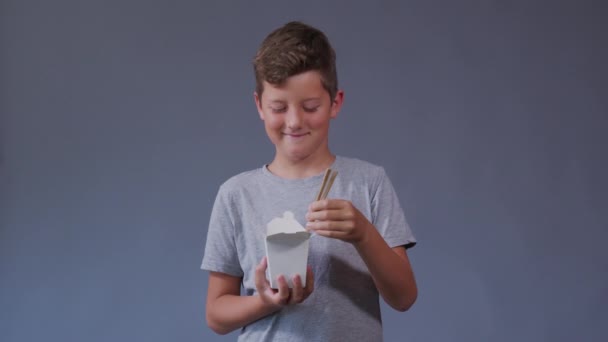 Boy relish is eating food. Smiling boy holding white box with chinese noodles. — Stock Video