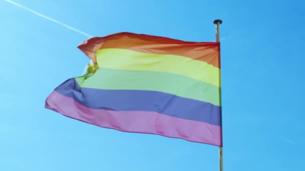 Μεγάλη σημαία Rainbow gay υπερηφάνεια ΛΟΑΤΚΙ που αναπτύσσεται από τον άνεμο ενάντια στον γαλάζιο ουρανό. — Αρχείο Βίντεο