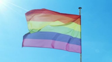 Büyük Gökkuşağı bayrağı gay gururu LGBTQ rüzgar tarafından mavi gökyüzüne karşı gelişiyor.